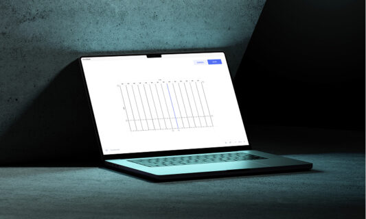 Open laptop on a dark surface displaying a design or layout editing interface on screen.